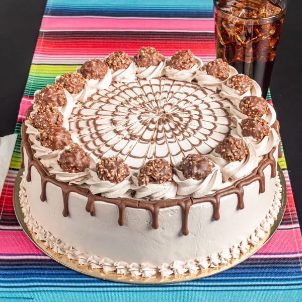 A chocolate cake with frosting, chocolate drizzle, and chocolate candies, next to a glass of soda.