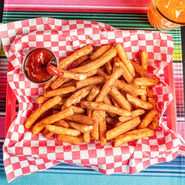 Seasoned french fries in a red basket with checkered paper, served with ketchup and a drink.