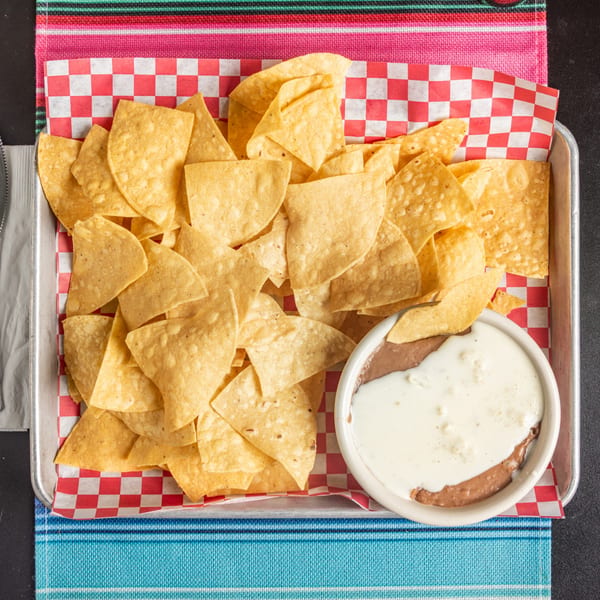 A tray of golden tortilla chips with a side of refried beans and white queso dip.