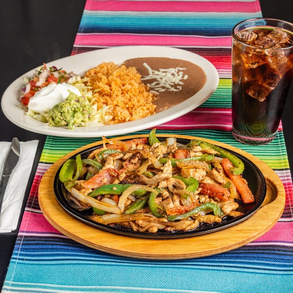 Sizzling chicken fajitas with bell peppers and onions, served with rice, beans, and a drink.